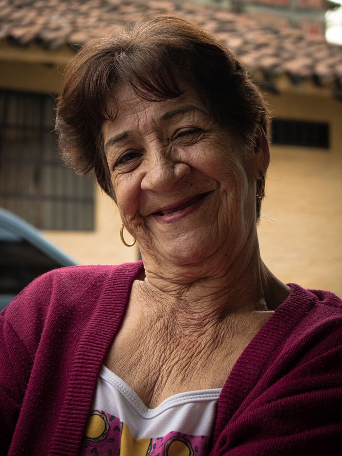 Mujer mayor sonriendo frente a su casa, en un barrio de Cali.