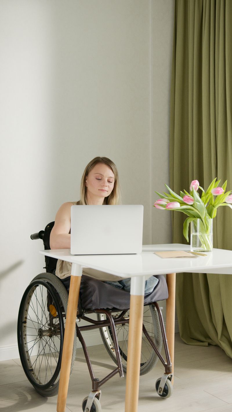 Mujer usuaria de silla de ruedas trabajando en su computador en un espacio adaptado.